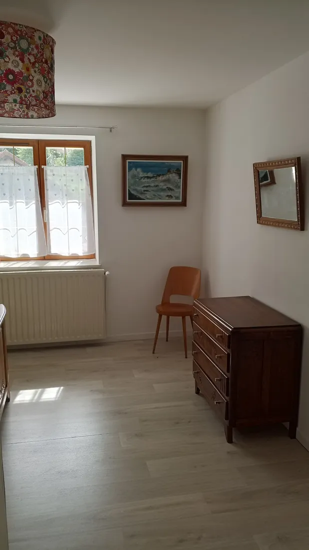 Seconde chambre avec commode en bois et grande fenêtre